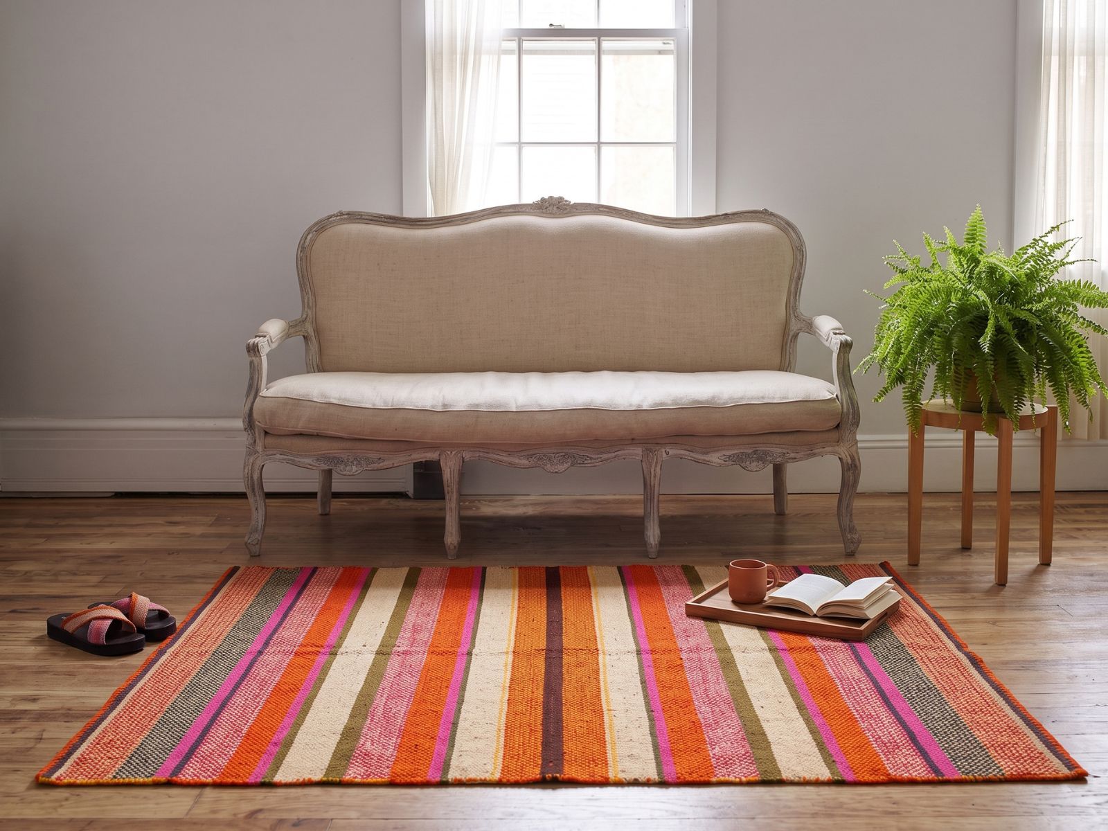 A vintage Peruvian frazada laid flat as a rug on aged timber floors in front of an ornate ivory sofa — Orange Inca
