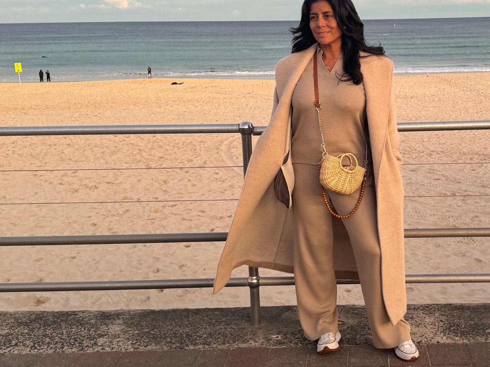 Woven junco bag styled for winter — camel coat and monochromatic outfit at the beach
