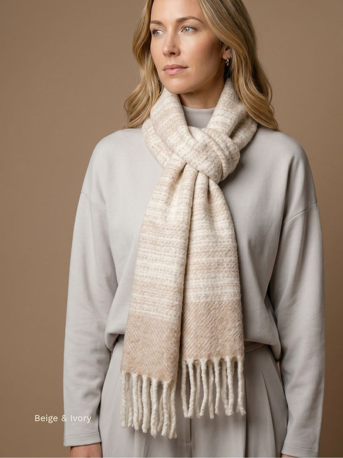 Woman wearing a beige and ivory striped bouclé baby alpaca scarf knotted at the neck over a grey sweater. Orange Inca