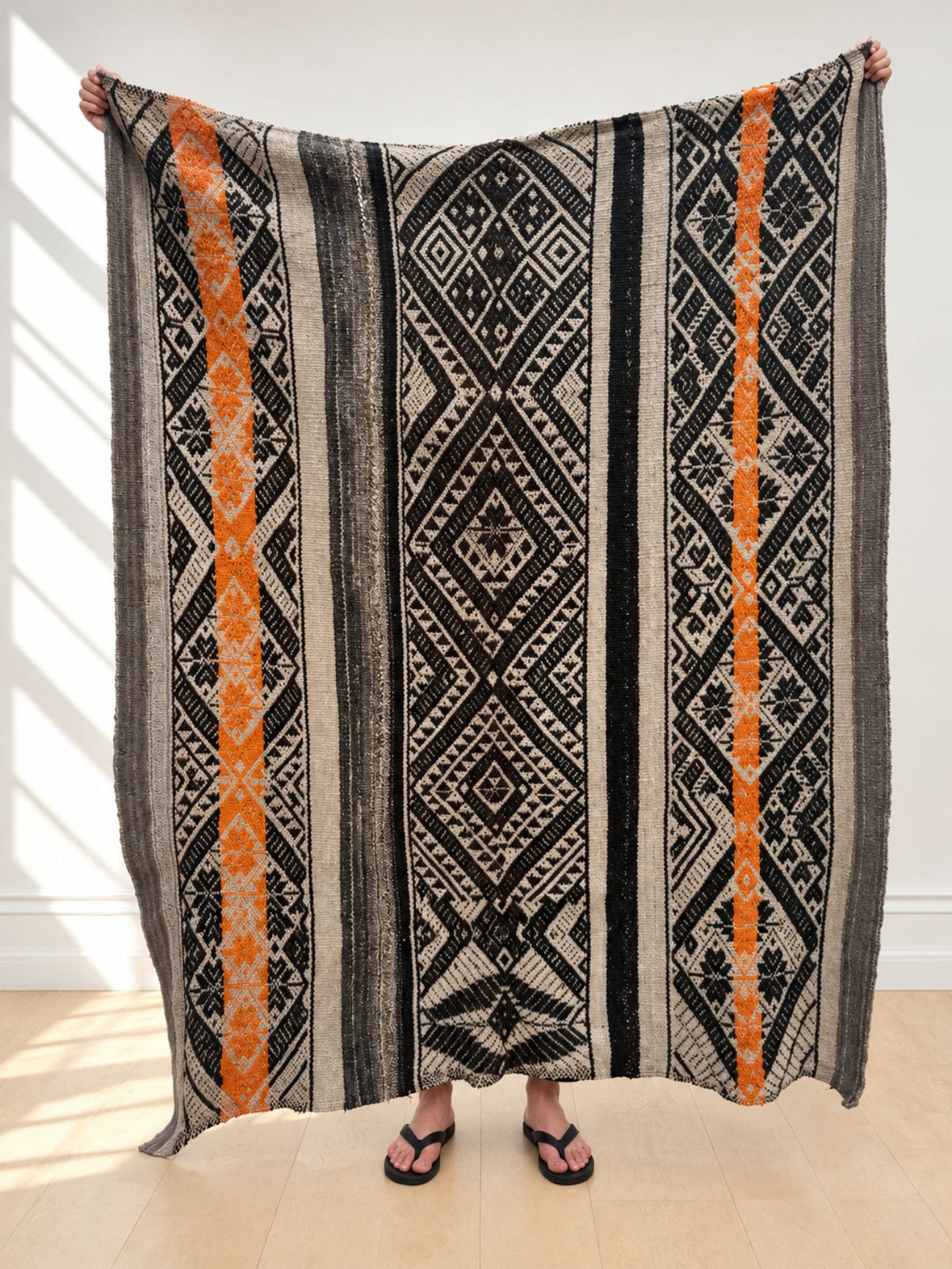 Vintage frazada rug No. 16 held up in full — charcoal, grey, cream and orange, handwoven Peruvian sheep and alpaca wool, 192 × 150 cm | Orange Inca