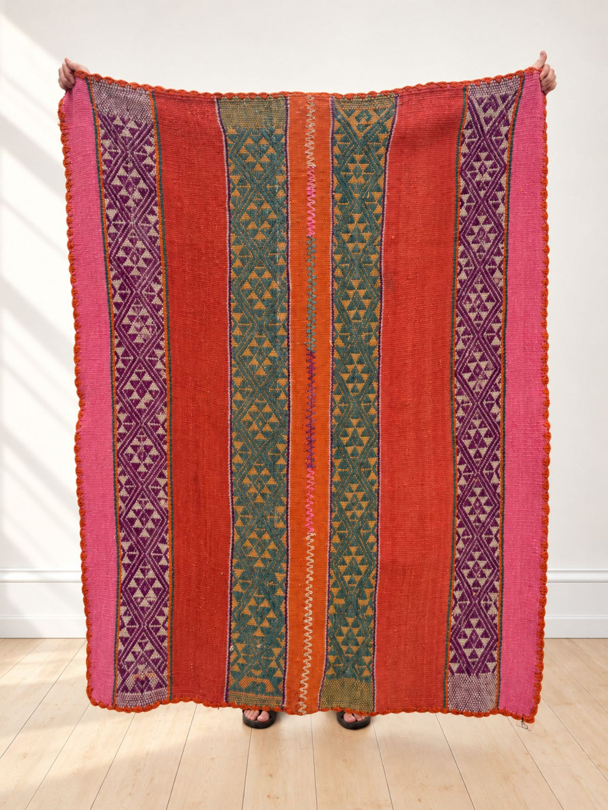 Vintage frazada rug No. 19 held up in full — red-orange field with pink, purple and teal triangle bands, handwoven Peruvian sheep and alpaca wool, 175 × 141 cm | Orange Inca