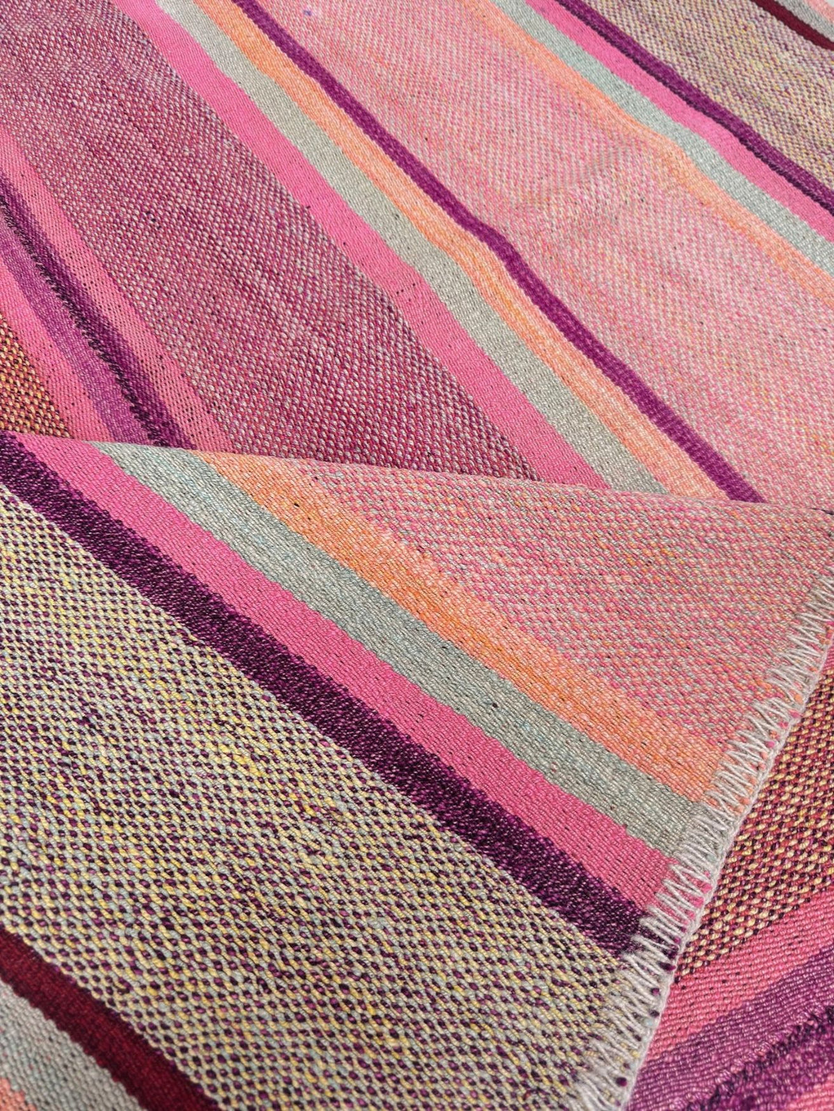 Close-up of frazada rug No. 2 — folded edge showing the handwoven pink, plum, peach and sage stripes and fringed selvedge | Orange Inca