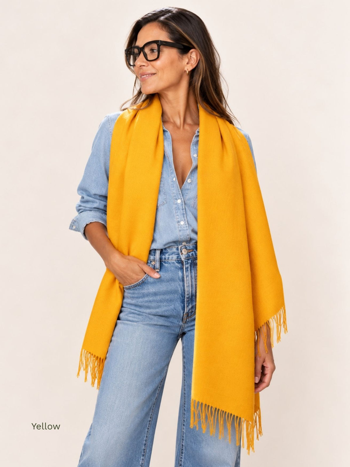 Woman wearing a yellow naturally dyed baby alpaca shawl draped around her shoulders with a denim shirt and jeans. Orange Inca