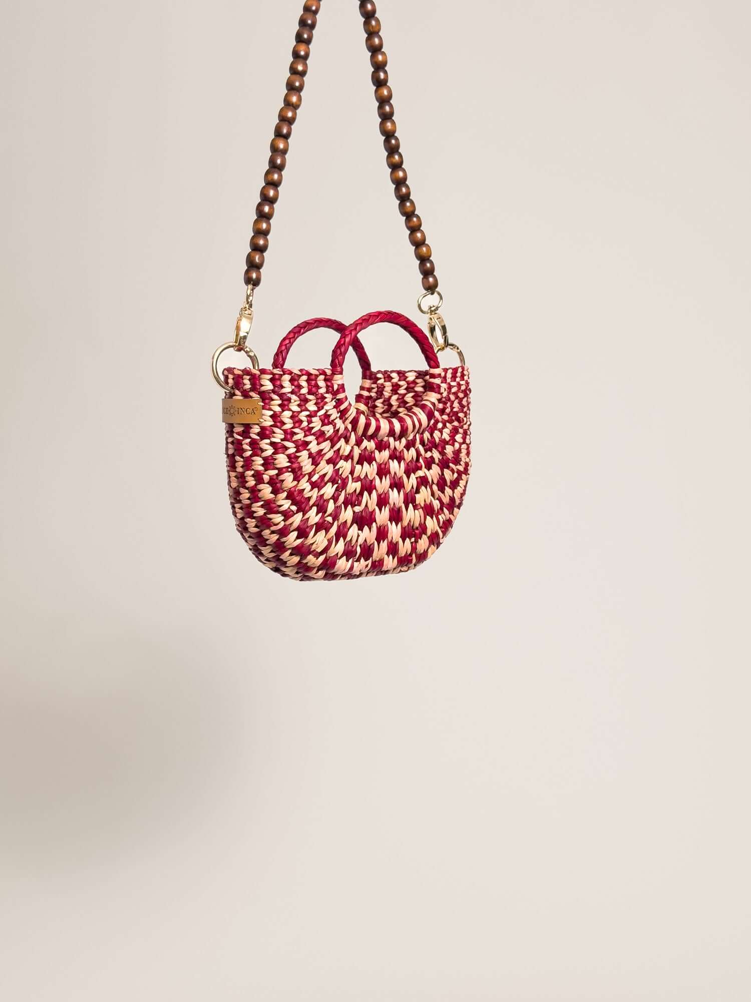 The Fiesta Mini Deluxe - Checkered Burgundy and Natural handwoven junco crossbody bag with wooden bead strap.