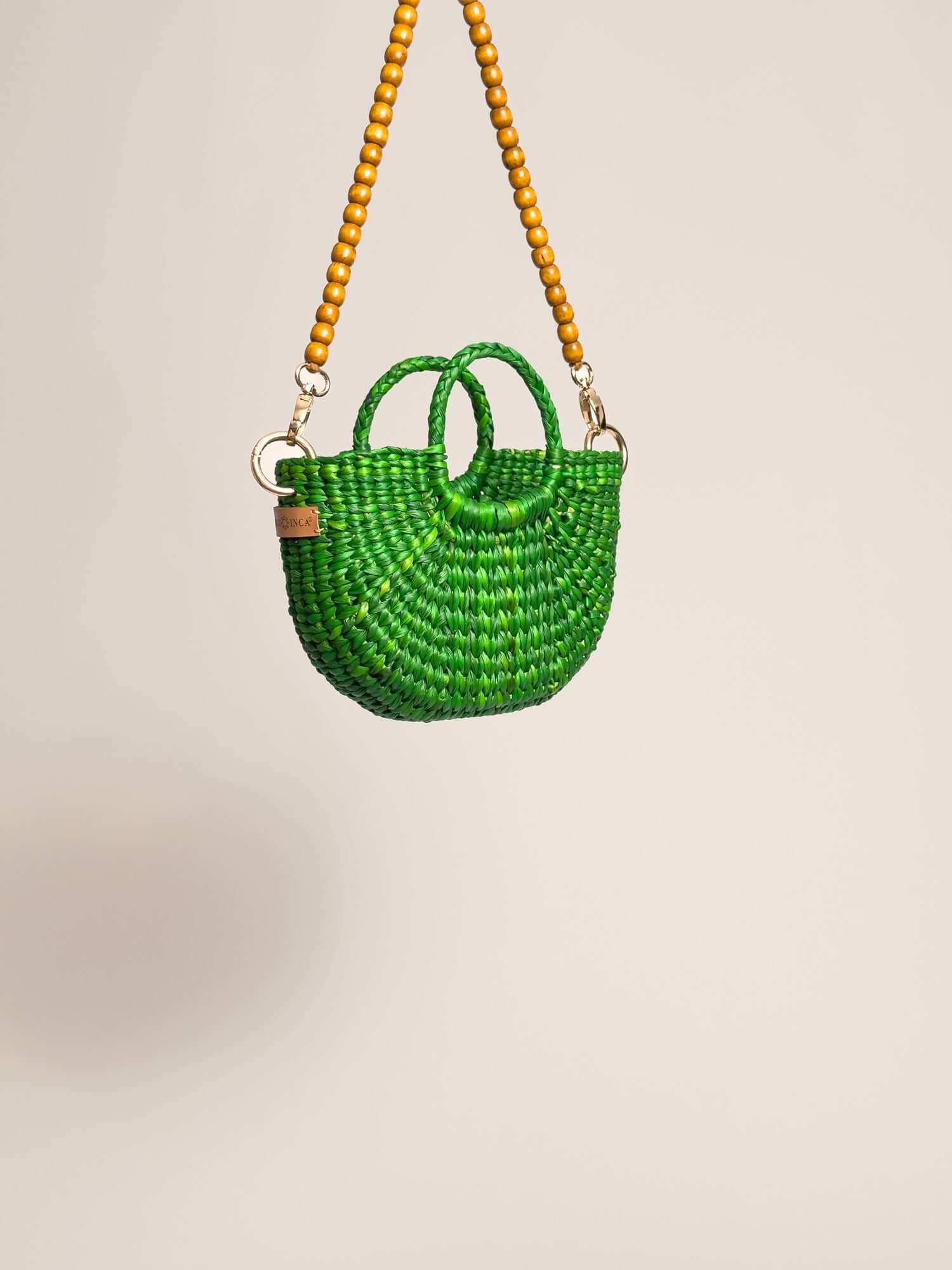 The Fiesta Mini Deluxe - Emerald Green handwoven junco crossbody bag with wooden bead strap and two handles.