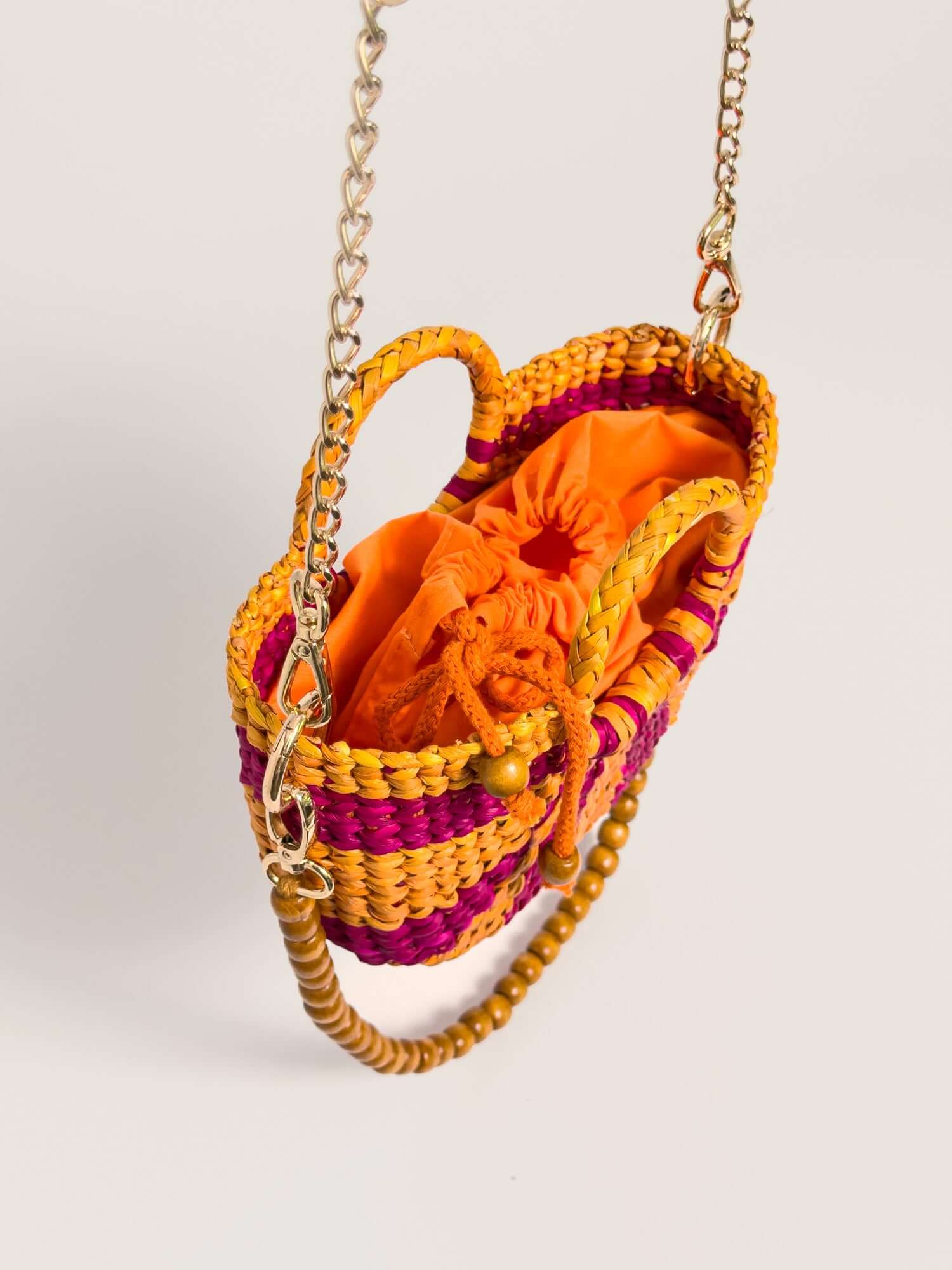 The Fiesta Mini Deluxe - Striped Fuchsia and Orange, handwoven junco crossbody bag with chain strap and orange interior.