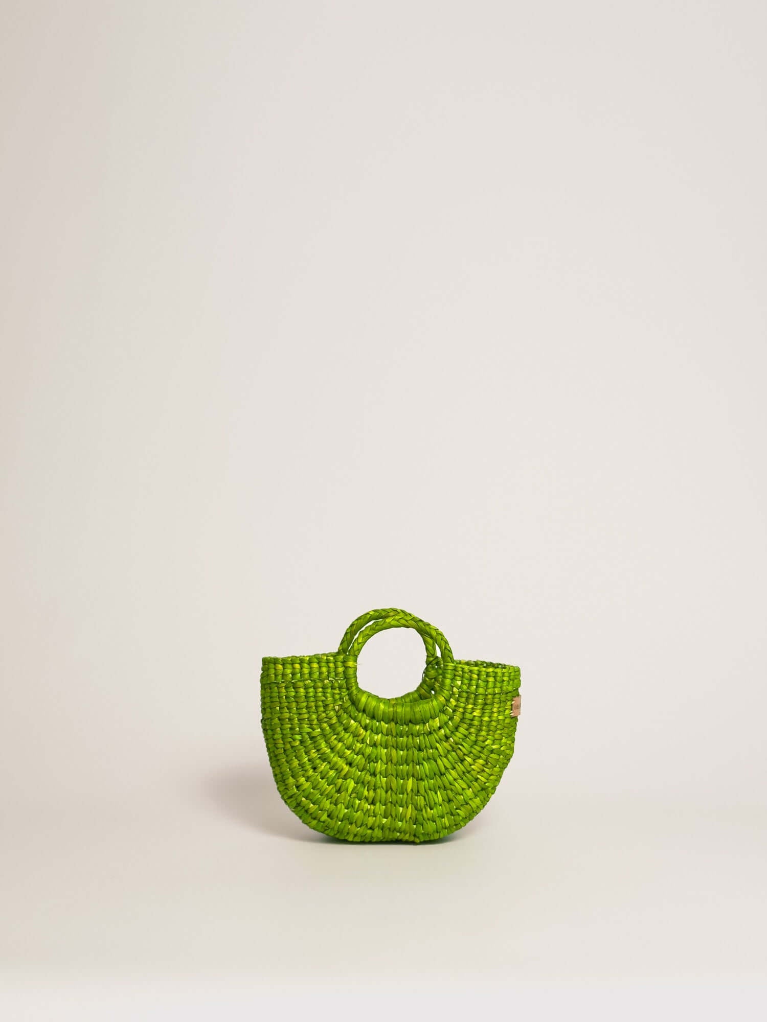 The Fiesta Mini Deluxe - Lime Green handwoven junco crossbody bag with a circular handle and natural fibre construction.