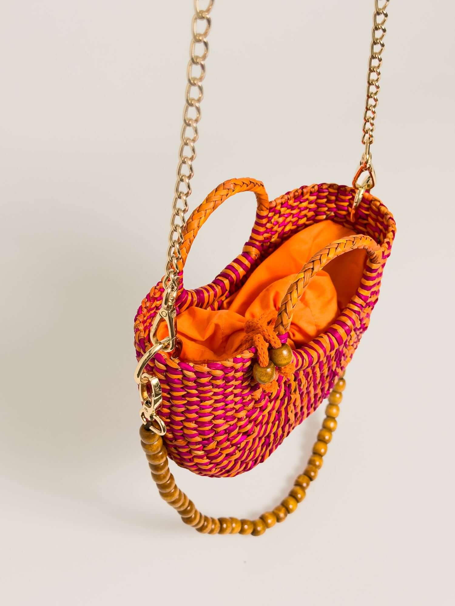 The Fiesta Mini Deluxe - Marbled Fuchsia and Orange handwoven junco crossbody bag with chain strap and wooden beads.