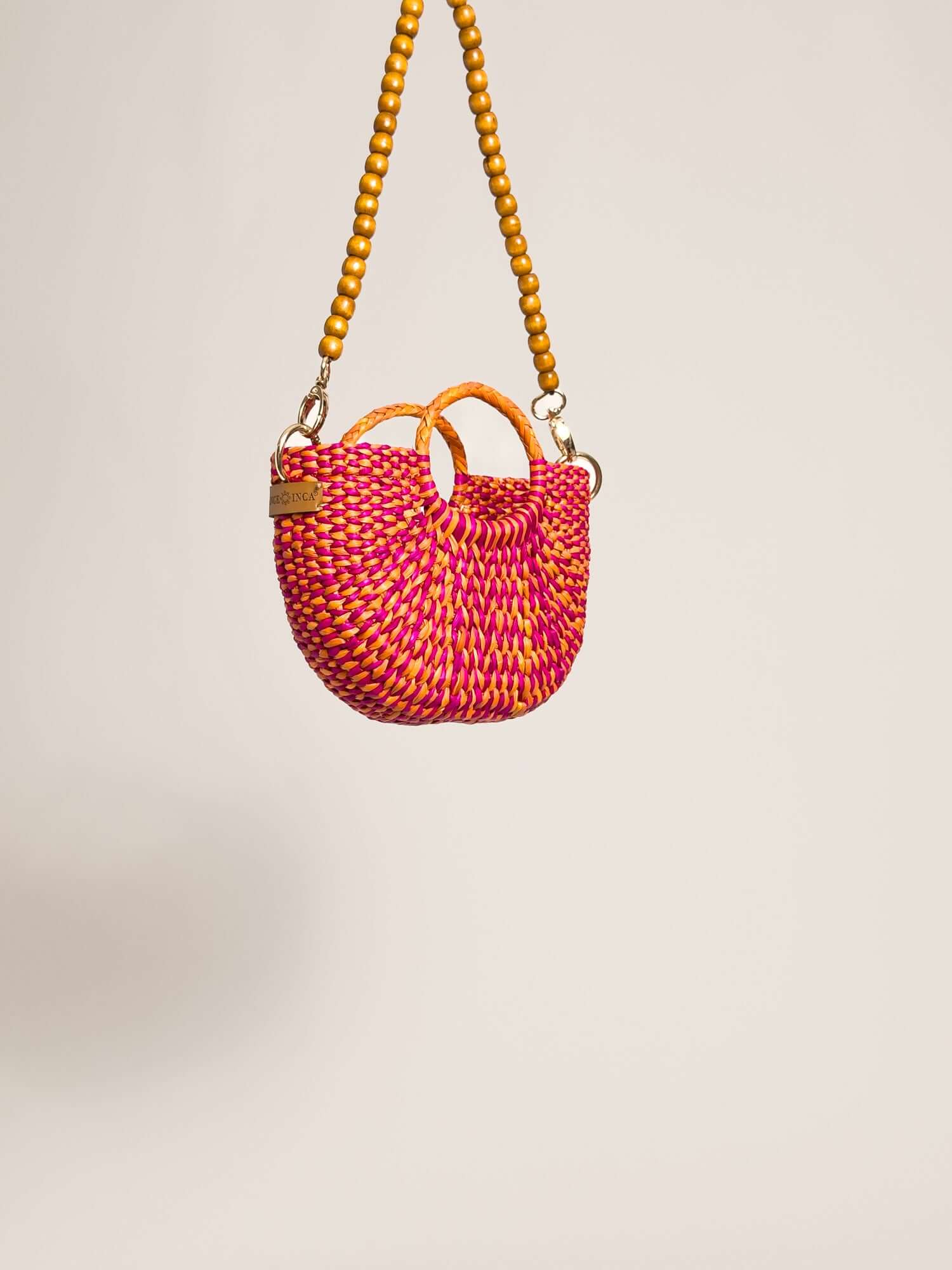 The Fiesta Mini Deluxe - Marbled Fuchsia and Orange, handwoven junco crossbody bag with wooden beads strap and leather handles.