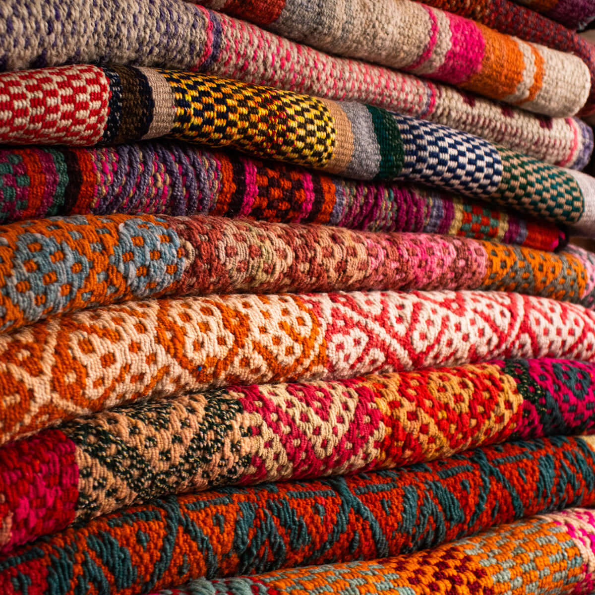 Stack of colourful frazadas showcasing rich Peruvian patterns and craftsmanship.