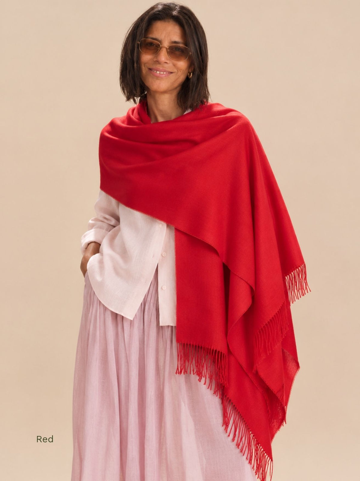 Woman wearing a red silk baby alpaca blend shawl draped over one shoulder with a white shirt and pink skirt. Orange Inca