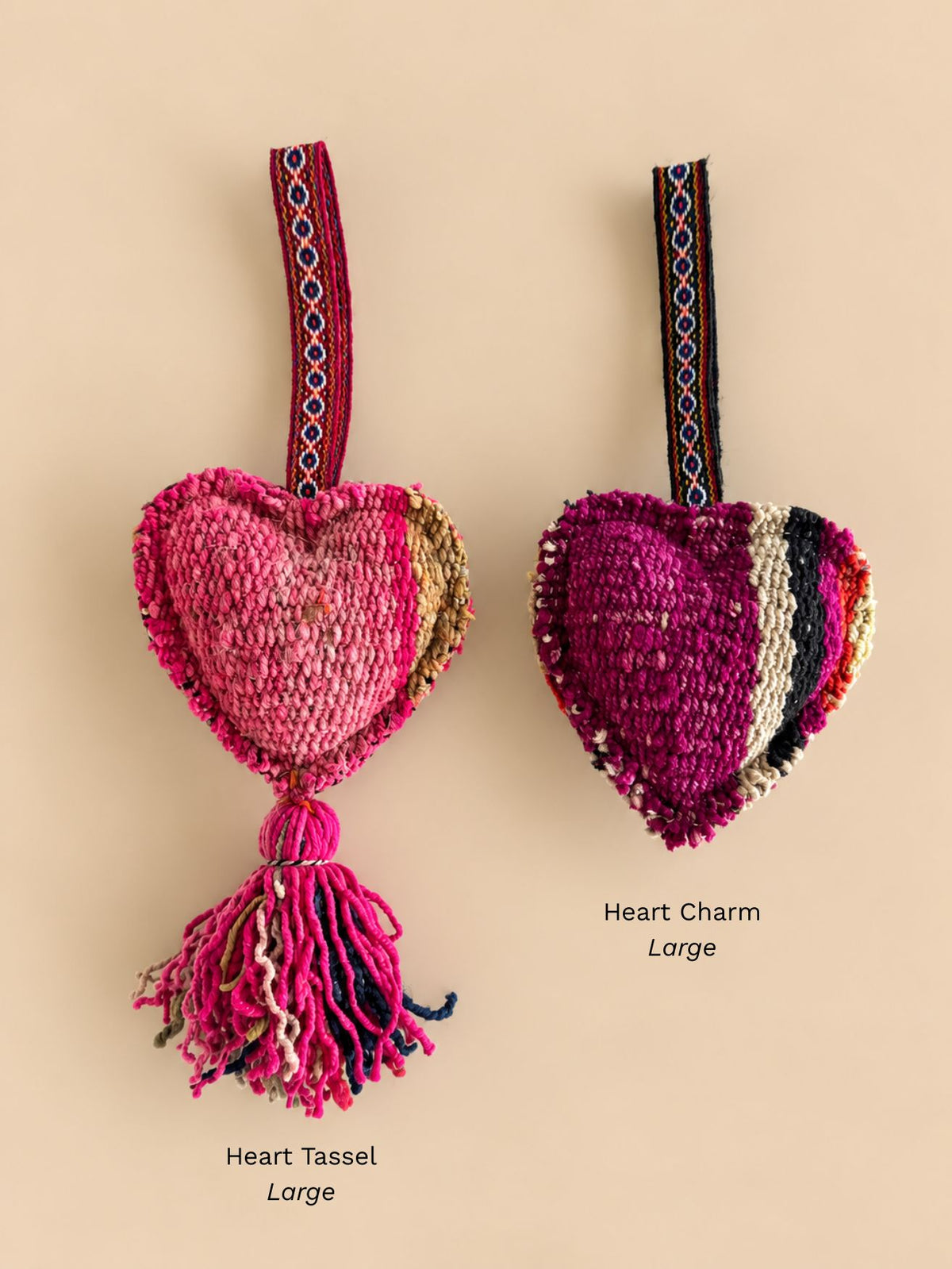 Large heart wool tassel in pink, fuchsia and tan next to a large magenta heart wool charm with cream and black stripes, labelled Heart Tassel Large and Heart Charm Large | Tasselita by Orange Inca