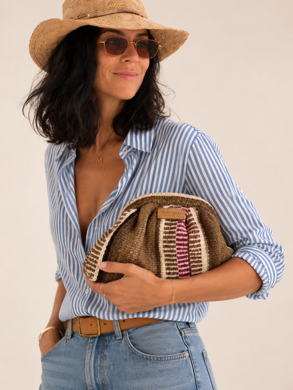 Woman in a blue striped shirt and straw hat holding the Luna kiss lock clutch in browns, ivory and burgundy | Orange Inca