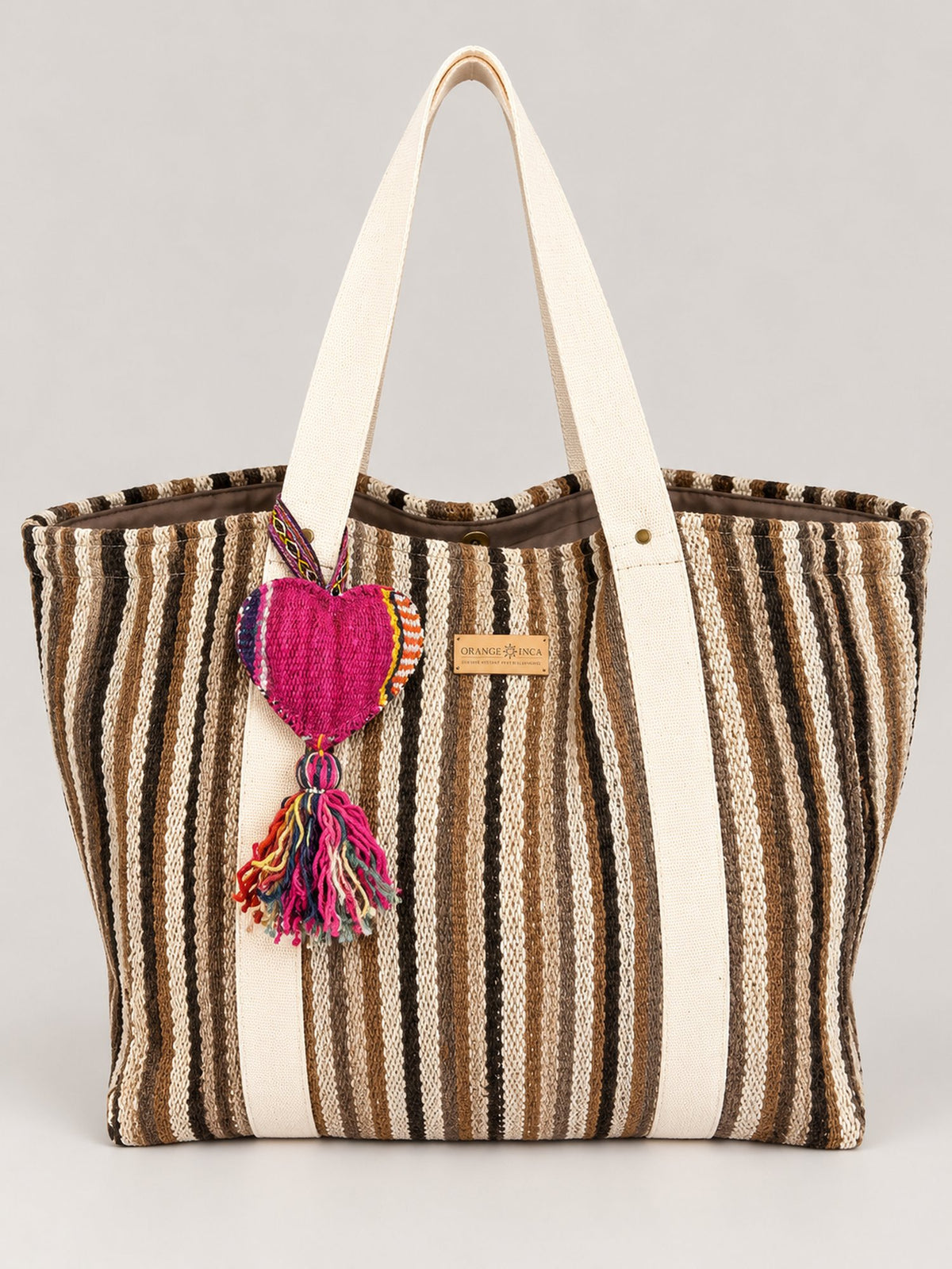 The Manta Carryall in Brown and Cream Stripes — front, with a wool tassel bag charm