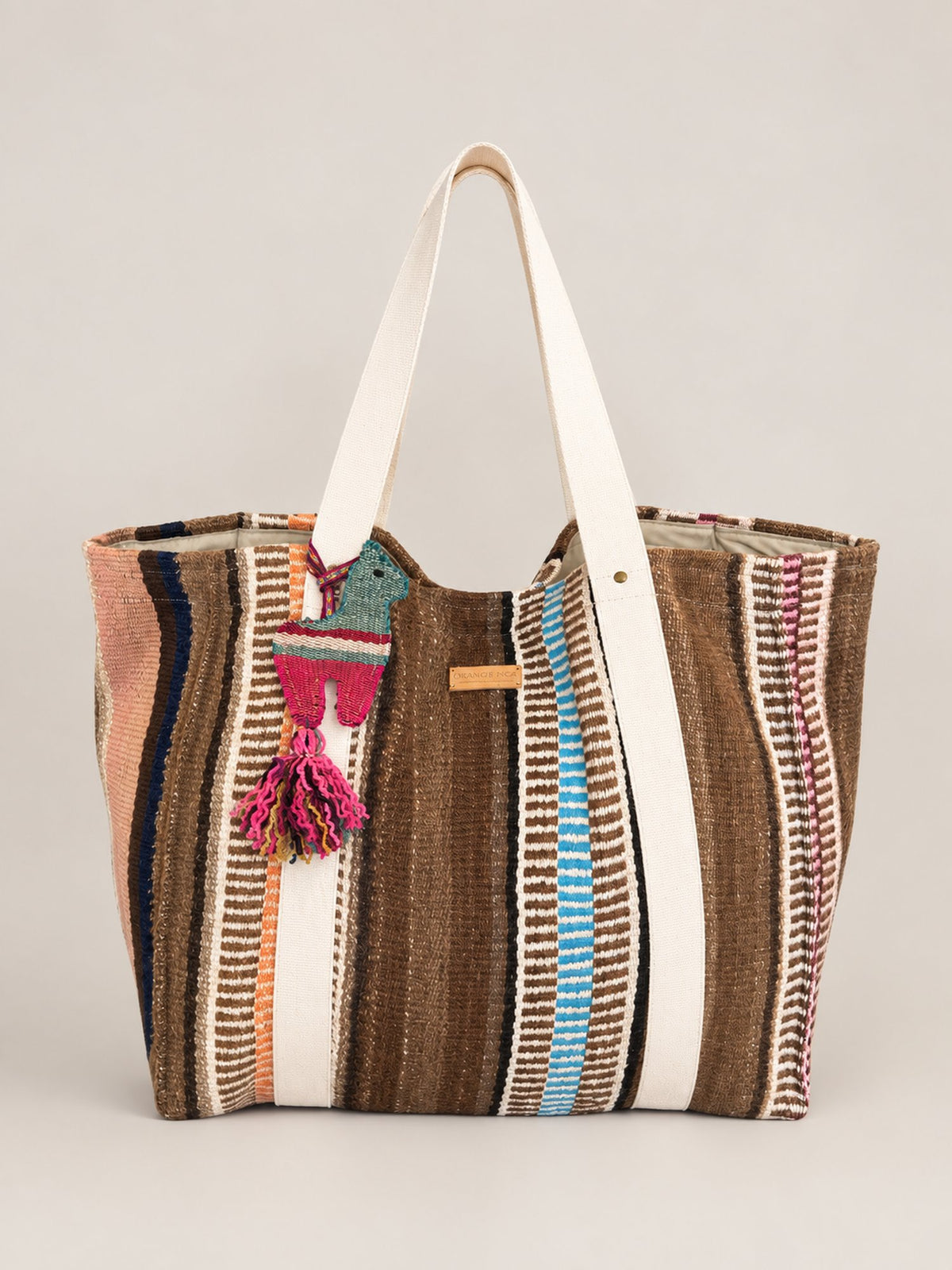 The Manta Carryall in Browns, Peach and Sky Blue — front, with a wool tassel bag charm
