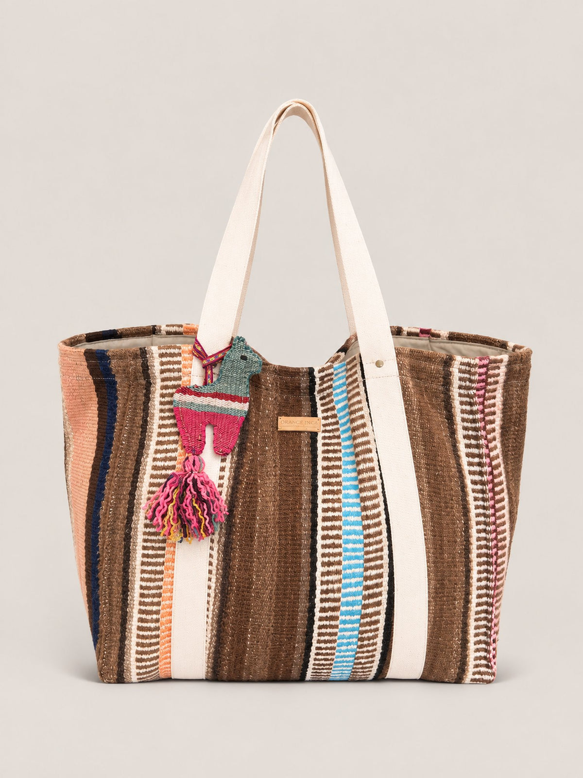 The Manta Carryall in Browns, Peach and Sky Blue — with a wool tassel bag charm, angled view