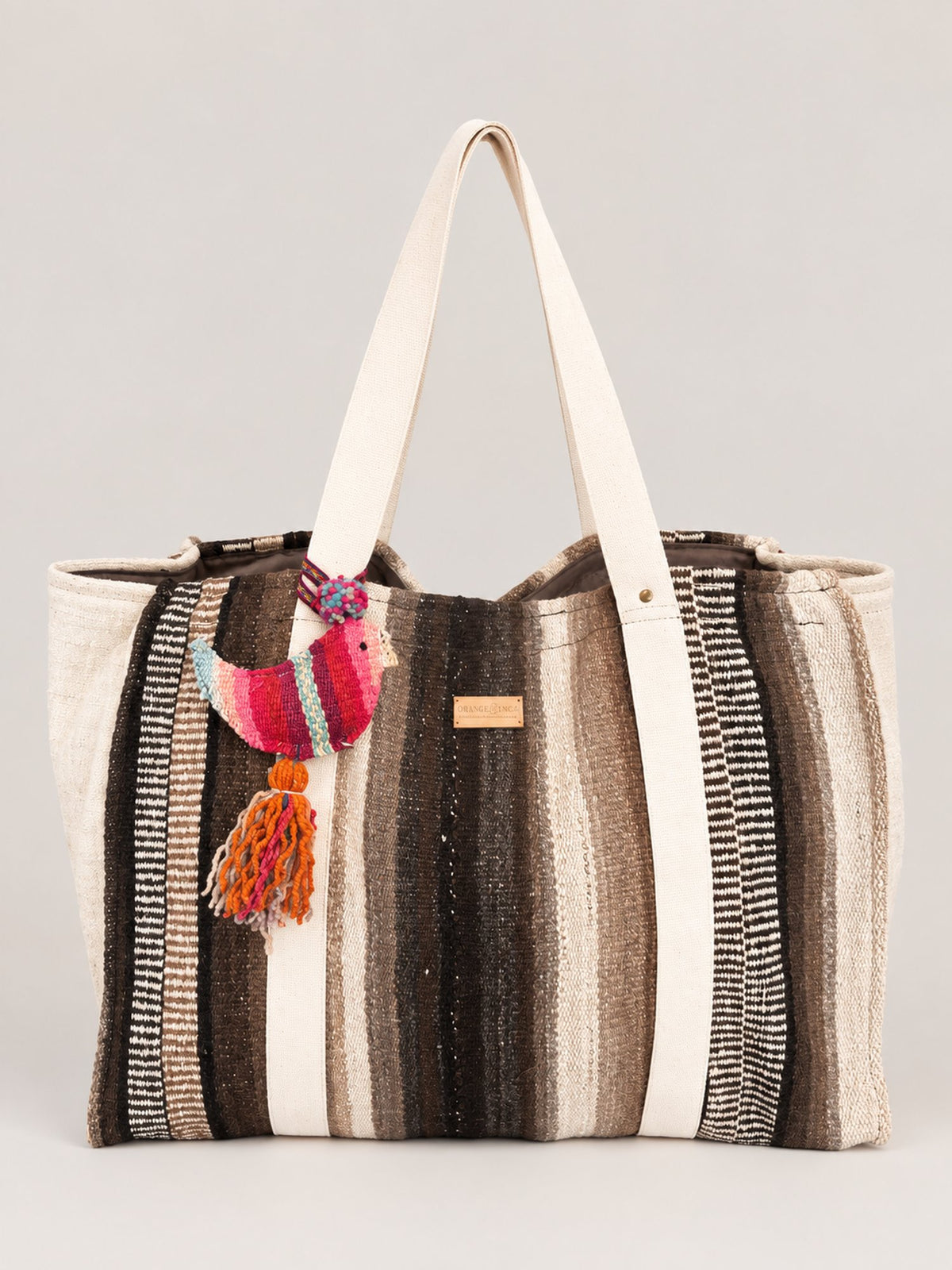 The Manta Carryall in Dark Browns and Ivory — front, with a wool tassel bag charm