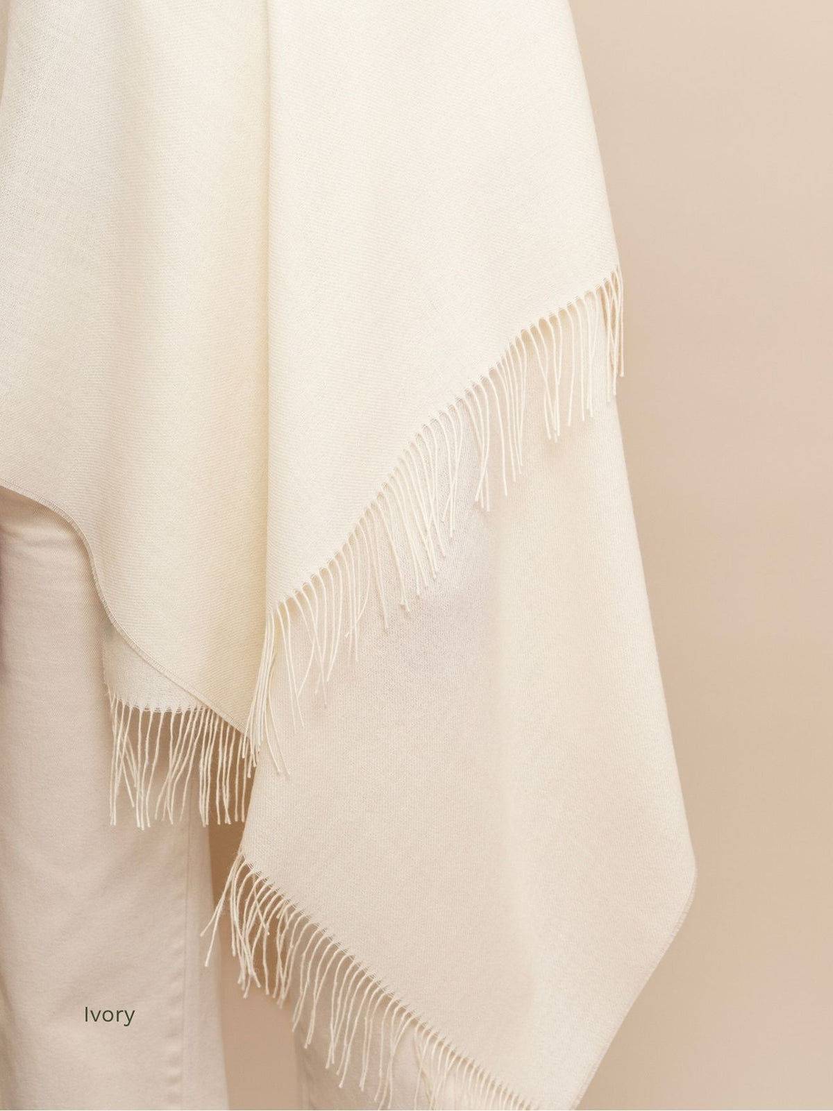 Ivory undyed baby alpaca shawl draped over cream trousers, showing the soft drape and long twisted fringe