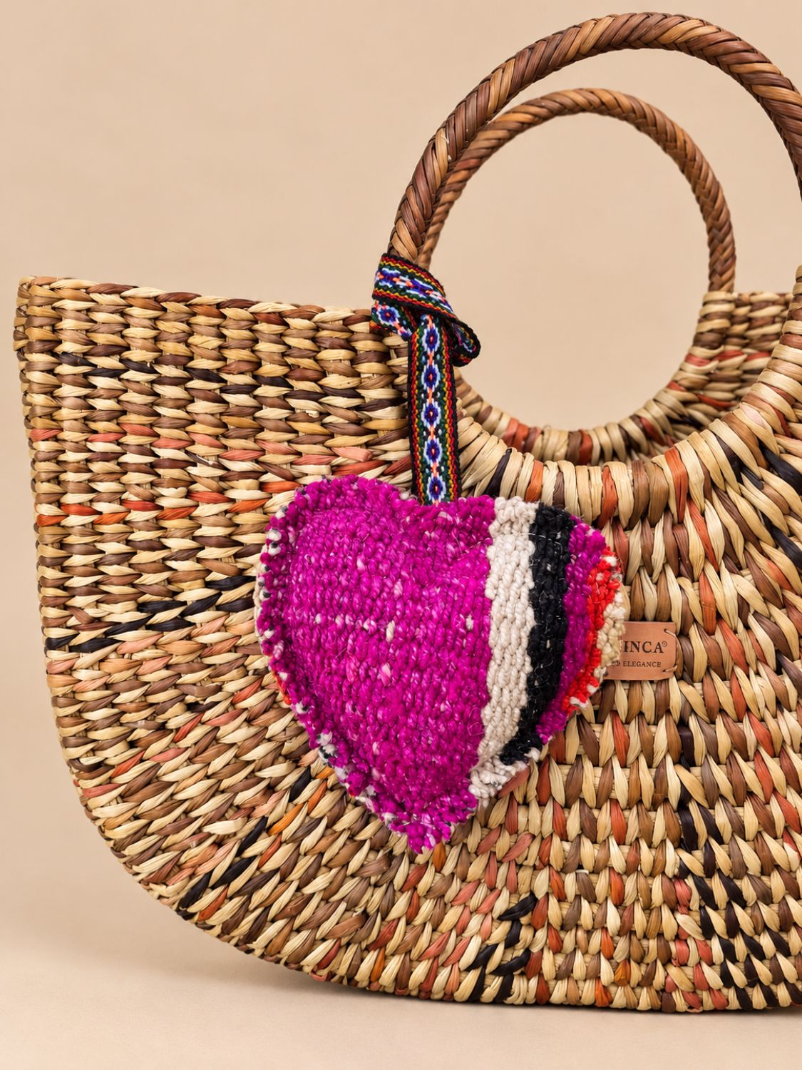 Large heart wool charm tied to the handle of a woven straw bag | Tasselita by Orange Inca