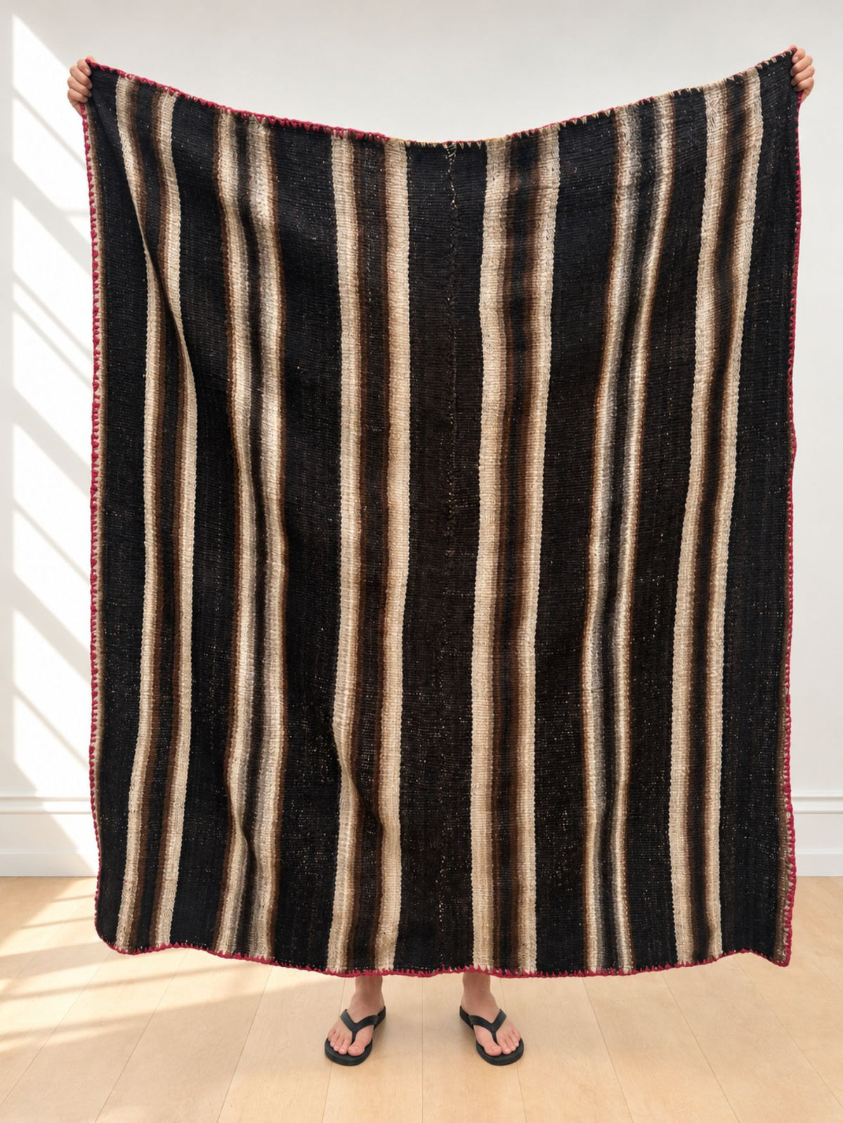 Vintage frazada rug No. 17 held up in full — black, cream and soft brown, handwoven Peruvian sheep and alpaca wool, 177 × 150 cm | Orange Inca