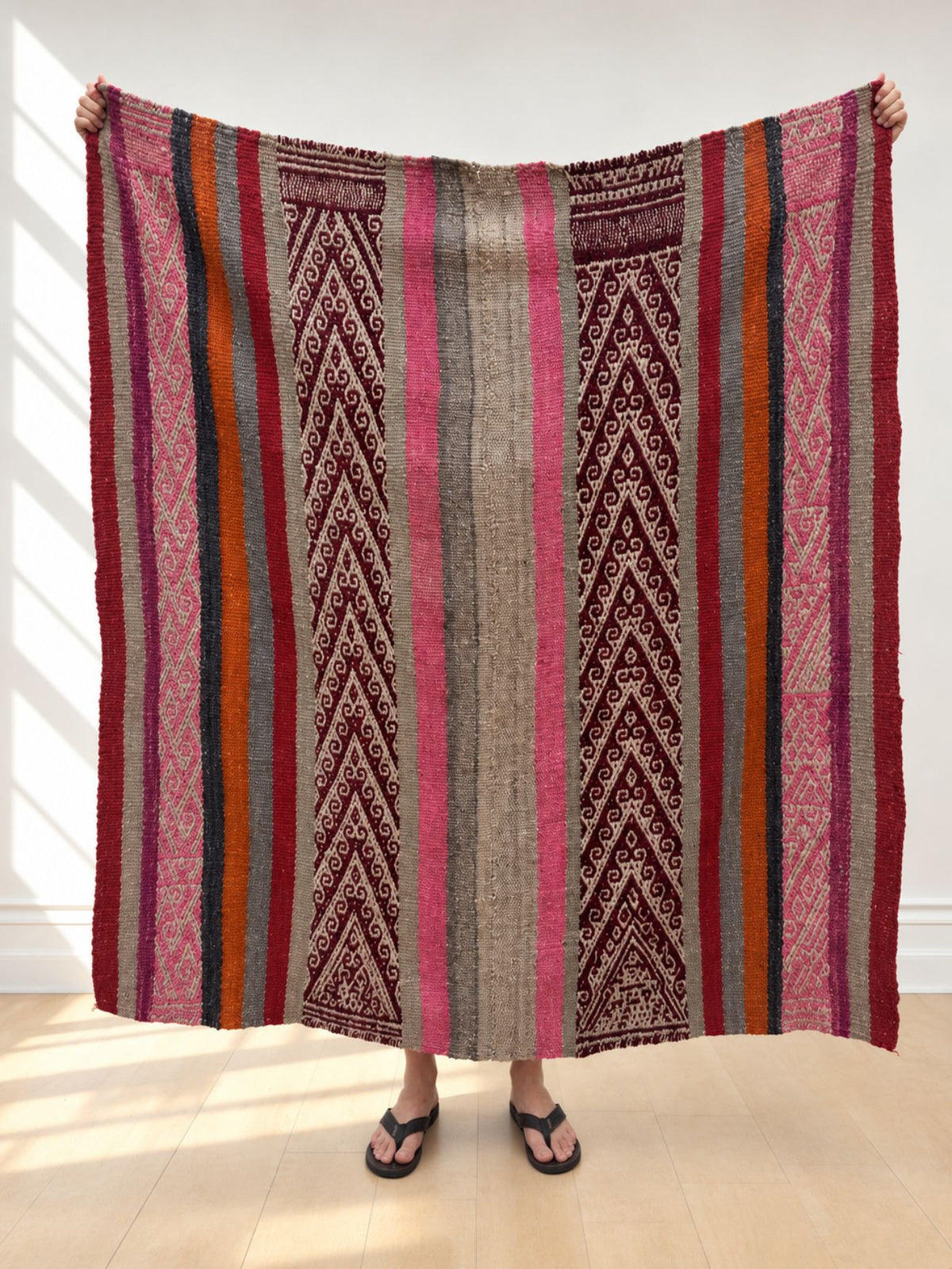 Vintage frazada rug No. 20 held up in full — burgundy chevron bands with pink, grey and orange stripes, handwoven Peruvian sheep and alpaca wool, 153 × 152 cm | Orange Inca