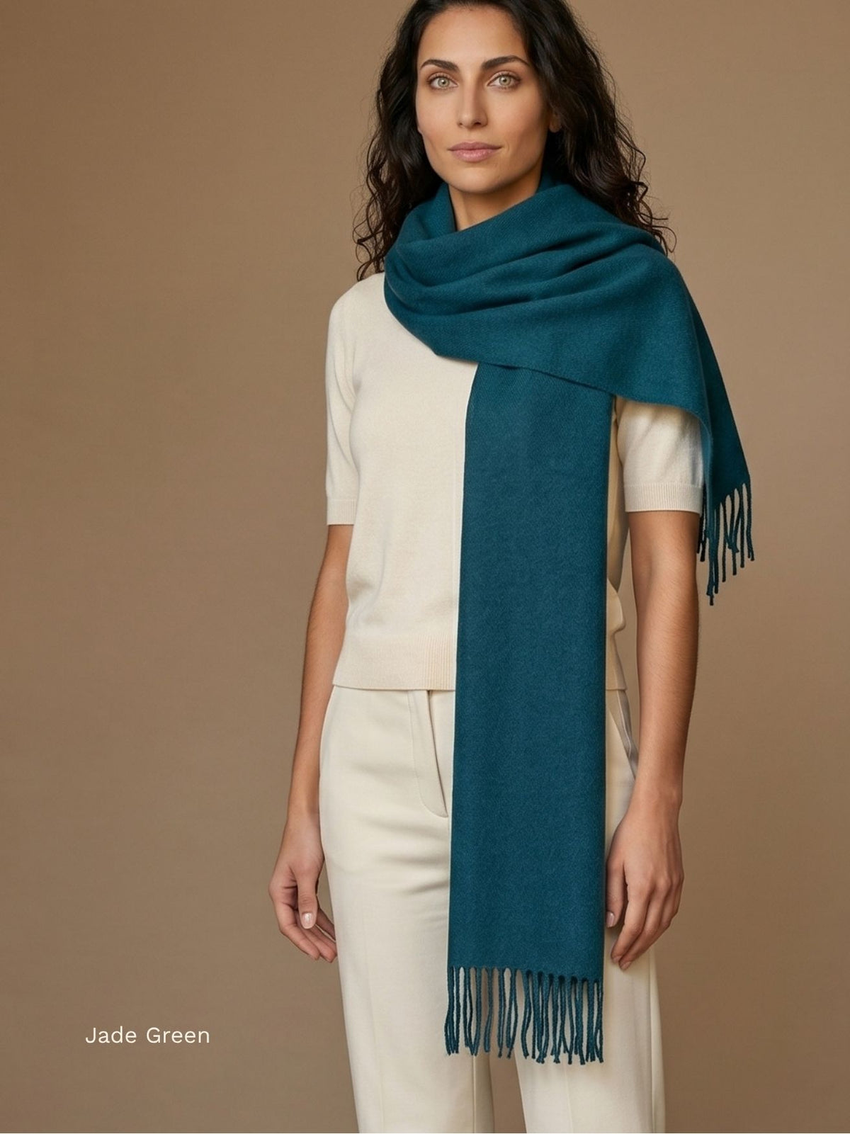 Woman wearing a jade green naturally dyed baby alpaca scarf draped over a cream top and trousers, fringed ends. Orange Inca