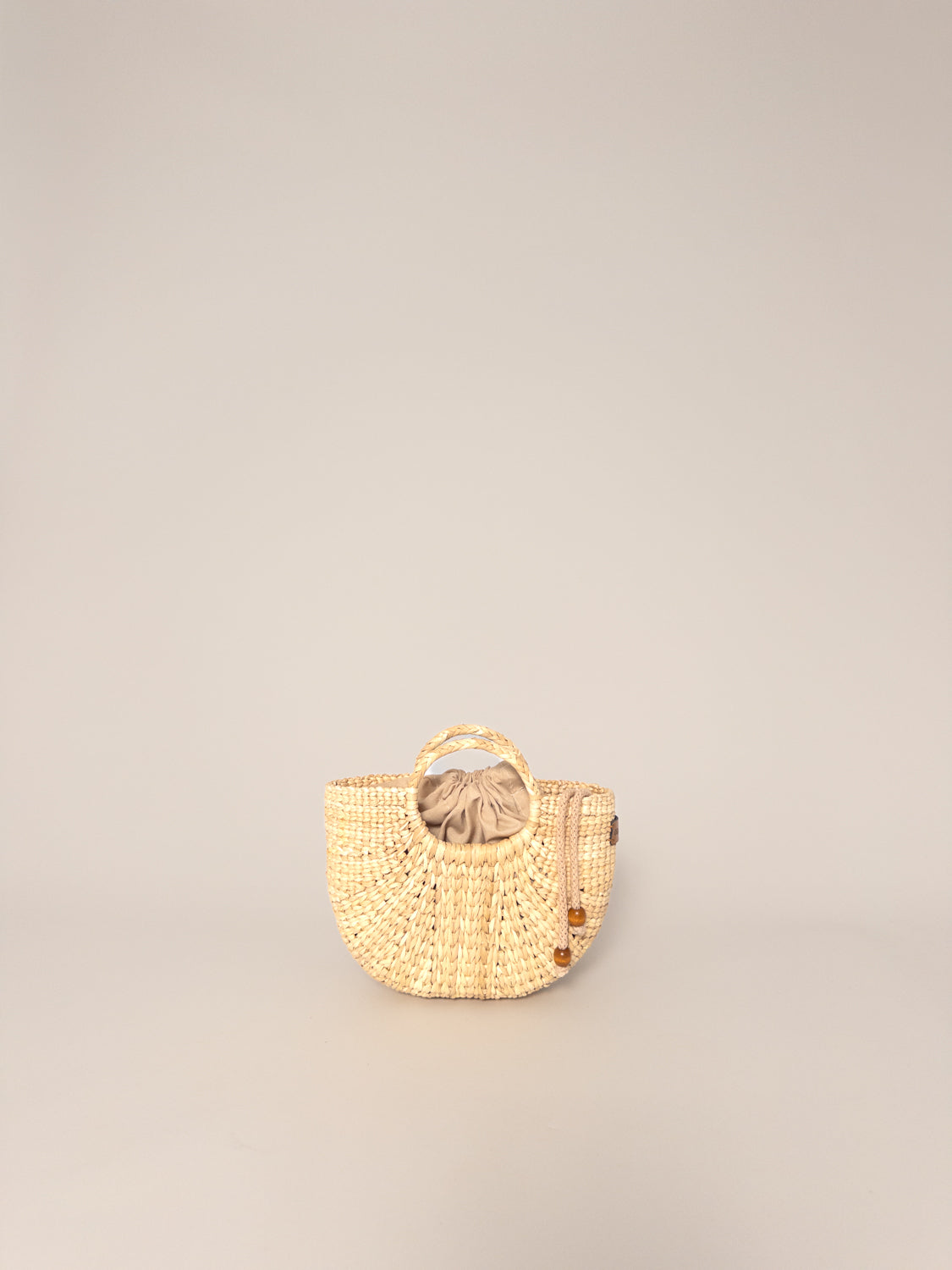 The Fiesta Mini Deluxe - Natural, handwoven junco crossbody bag, beige, round shape, top handle, lightweight design.