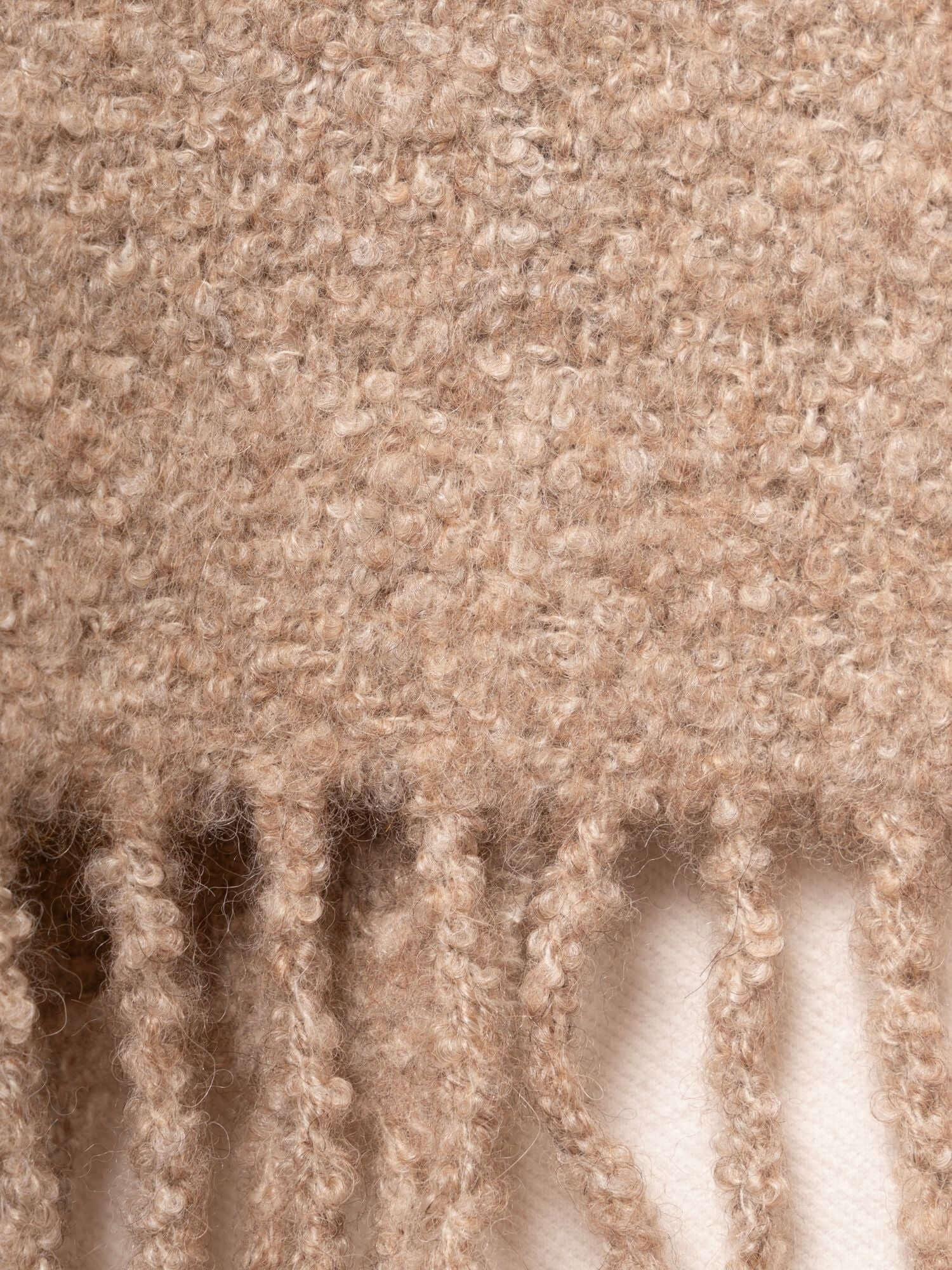 Close-up of twisted fringes on undyed bouclé alpaca silk scarf, showing soft oatmeal yarn texture