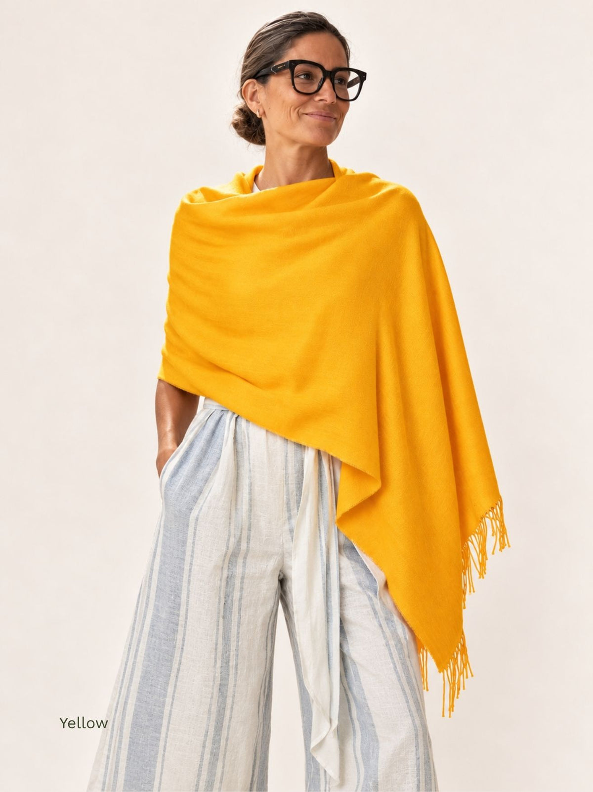 Woman wearing a yellow silk baby alpaca blend shawl wrapped around the shoulders with striped linen trousers