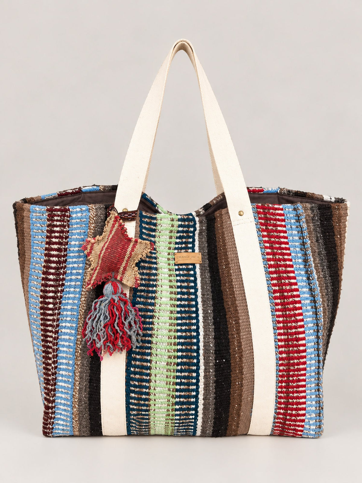 The Manta Carryall in Blue, Green and Berry Stripes — front, with a wool tassel bag charm