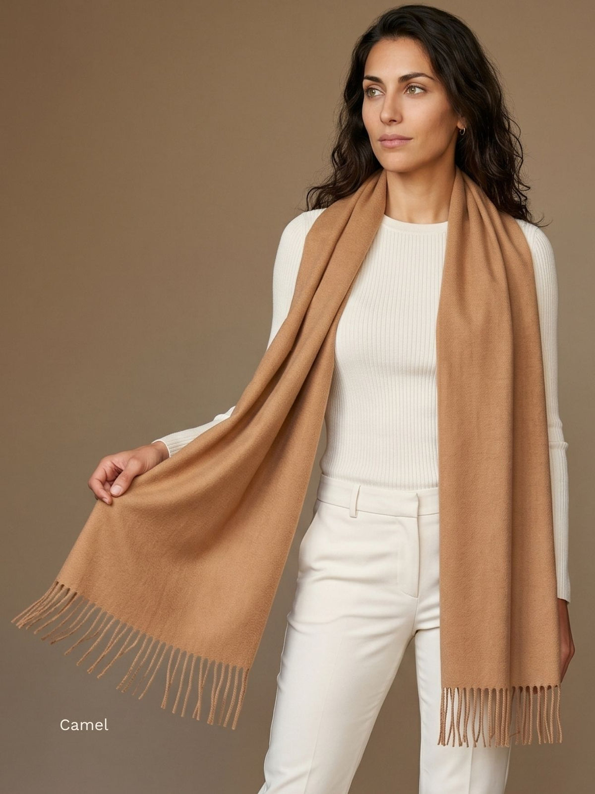 Woman wearing a camel undyed baby alpaca scarf draped long over a cream top and trousers, holding the fringed end. Orange Inca