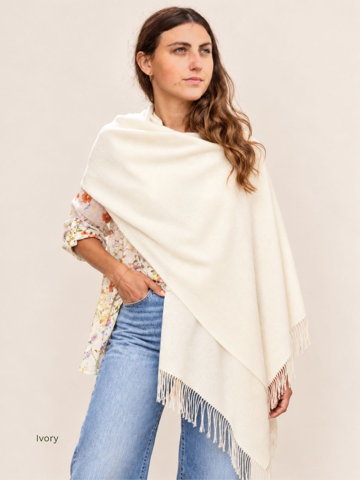 Woman wearing an ivory undyed baby alpaca shawl draped over one shoulder with jeans, long twisted fringe. Orange Inca, made in Peru